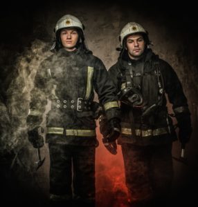 Two firefighters with helmet and axe in a smoke